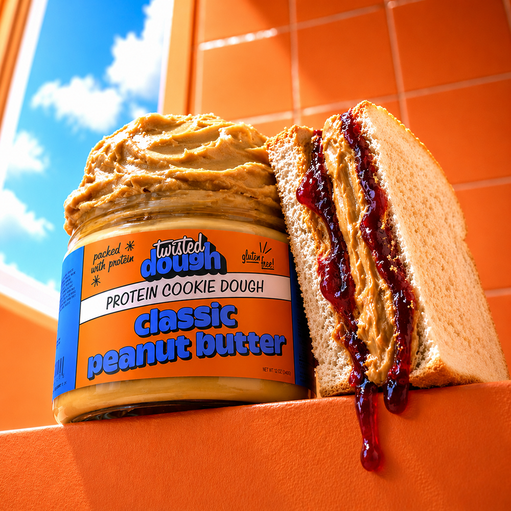 Twisted Dough peanut butter jar with a sandwich filled with peanut butter and jelly on an orange surface.