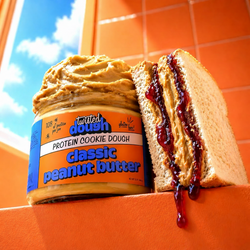 Person holding a spoonful of peanut butter over a blender with ingredients, next to a jar of peanut butter.