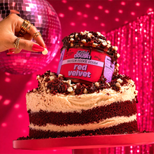 Load image into Gallery viewer, Red velvet cake with a container of Twisted Dough red velvet protein cookie dough on top, against a disco ball and curtain background.