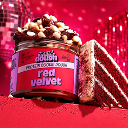 Red velvet cake with a container of Twisted Dough red velvet protein cookie dough on top, against a disco ball and curtain background.