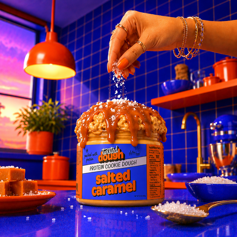 Person sprinkling toppings on a jar of salted caramel cookie dough in a kitchen setting.