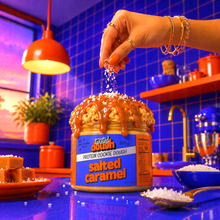 Load image into Gallery viewer, Person sprinkling toppings on a jar of salted caramel cookie dough in a kitchen setting.